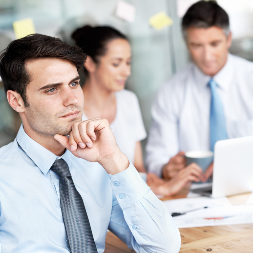 Two people are at a table in an office setting in the background, and one man is on the side, thinking about How to Financially Prepare For A Midlife Career Change.